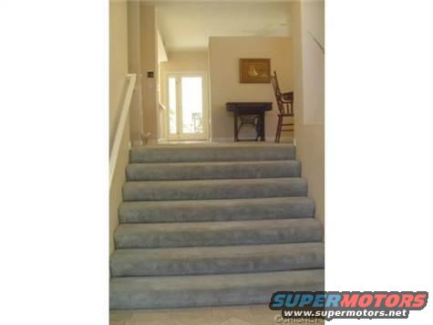 Interior staircase with grey carpet leading to a doorway and a wooden chair