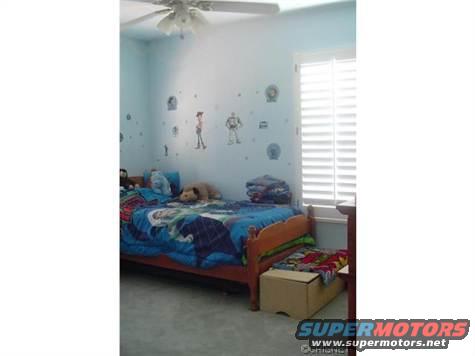 Child's bedroom with a twin bed, blue bedding, and Toy Story wall decals. Window blinds are visible