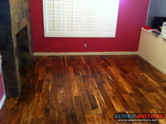 Interior room with hardwood floors, red walls, and white shutters over a window. A stone fireplace is on the left