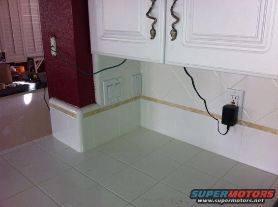 Kitchen counter with white tiled backsplash, red accent wall, and white cabinets. Electrical outlets and a black power adapter are visible