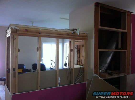 interior framing for a room addition, exposed studs, drywall, and some furniture visible through an opening