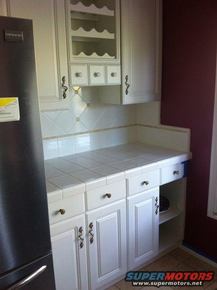 White kitchen cabinets with tiled countertop and a stainless steel refrigerator