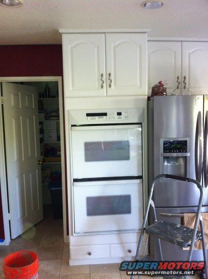 Kitchen scene with white cabinets, double oven, stainless steel refrigerator, and an open pantry door