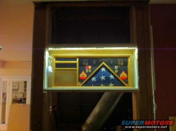 Shadow box with folded flag and military medals displayed in a wall niche