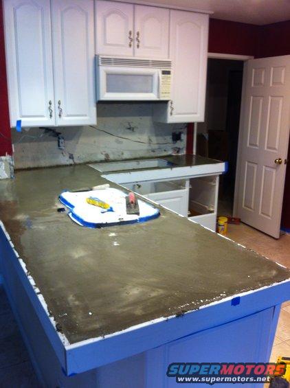 Kitchen countertop with wet concrete being troweled, cabinets and microwave above