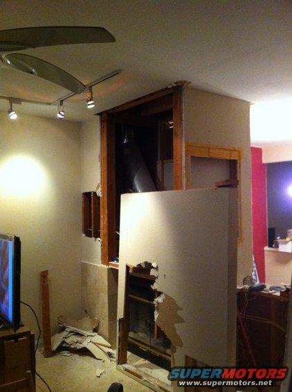 room under construction, fireplace opening exposed, drywall torn, fan on ceiling