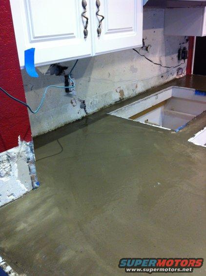 Wet concrete countertop with sink cutout, red wall, and white cabinets above