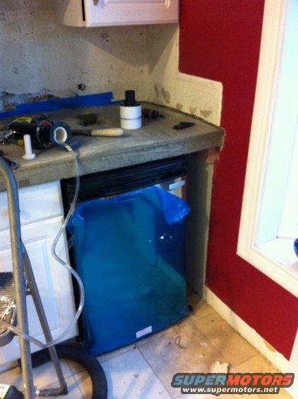 Countertop being installed, with tools and a blue trash bag underneath