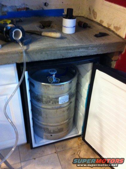 Beer keg inside mini-fridge with tubing connected. Tools and parts on counter above