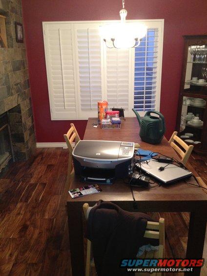 Dining room table with printer, laptop, watering can, and boxes