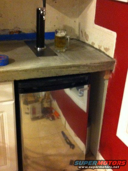 beer tap on counter next to mug of beer, mini-fridge below