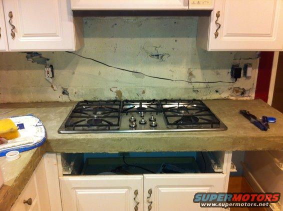 Kitchen countertop with a stainless steel gas stove, white cabinets, and exposed wiring