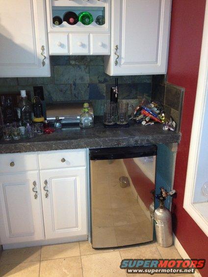 kitchen counter with bottles, shot glasses, beer mugs, a beer dispenser, and a mini-fridge. A CO2 tank is next to the fridge