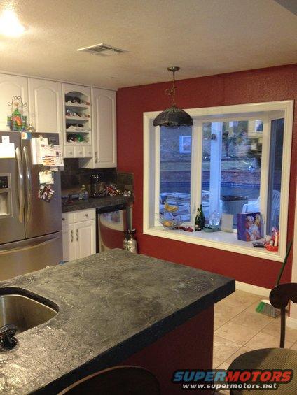 Kitchen with stainless steel refrigerator, white cabinets, dark countertop, and a bay window overlooking a backyard