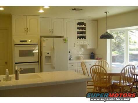 Kitchen with white cabinets, double oven, refrigerator, sink, and dining table with chairs by a large window