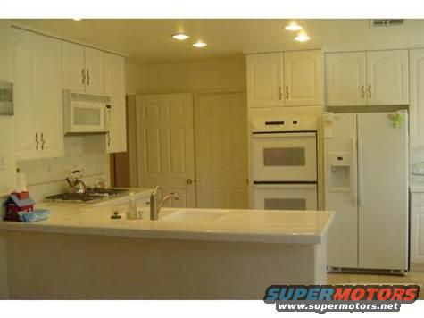 Kitchen with white cabinets, double oven, refrigerator, and sink