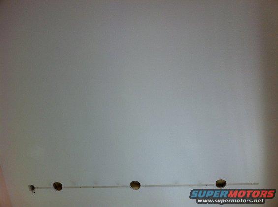 Wall with four holes and a thin metal strip running horizontally across them. Supermotors.net logo in lower right