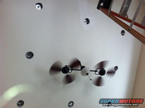 Ceiling fan with four blades, overhead view. Ladder in background