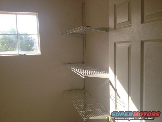 Interior view of a room with wire shelving on the wall and a window showing trees outside