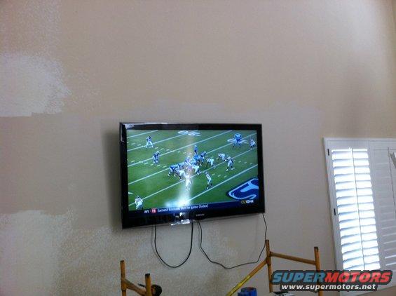 Television displaying a football game, mounted on a wall with scaffolding below