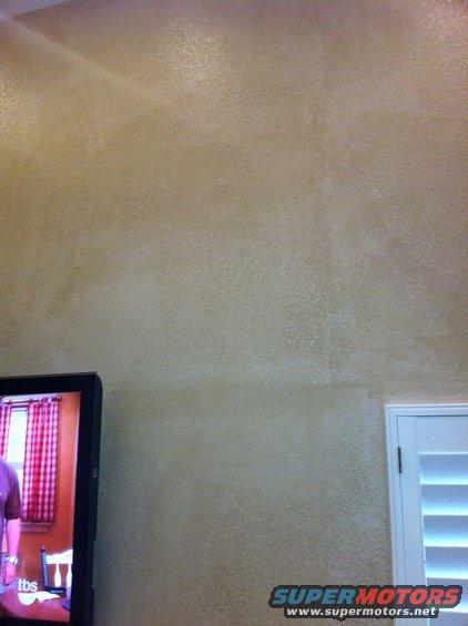 Interior wall with textured paint, a television displaying a person and checkered curtains, and a closed louvered door