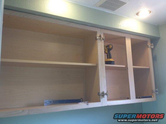 Empty kitchen cabinets with a drill on a shelf and a pry bar on the bottom shelf