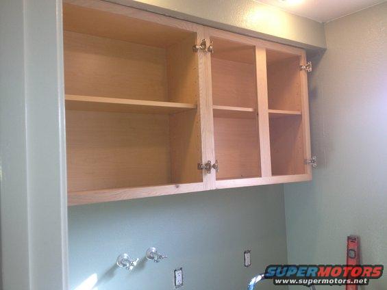 Unfinished kitchen cabinets with open doors, light wood interior, light green walls