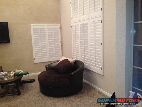 Living room with a large round chair, coffee table, and plantation shutters on the windows. Supermotors.net logo in the corner
