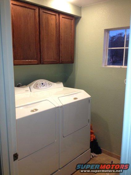 Laundry room with white washer and dryer, wood cabinets, and a small window