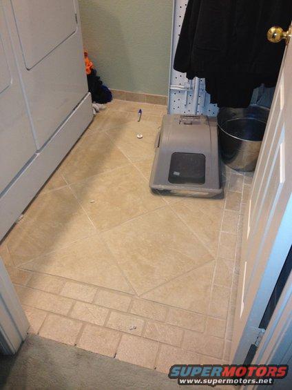 Laundry room with a white washing machine, a grey cat carrier, and a metal bucket