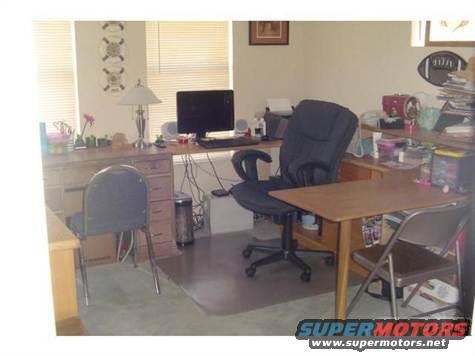 Office desk with computer, chairs, and shelves. A Supermotors.net watermark is visible
