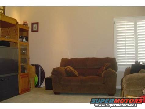 Living room interior with a brown sofa, a wooden entertainment center, and white window blinds