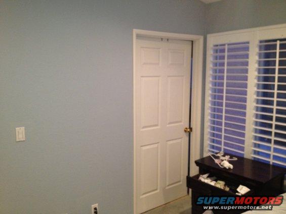 Interior room with a closed white door and white horizontal blinds on a window. A dark dresser is to the right