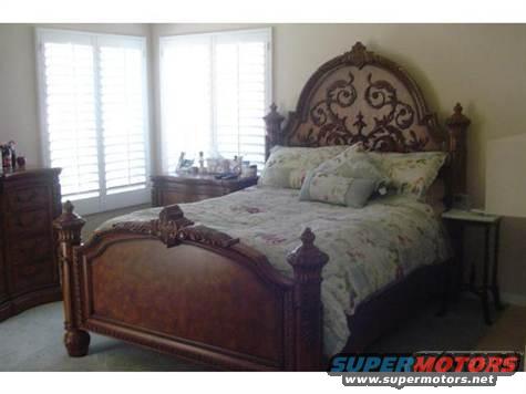 Bedroom with large ornate wooden bed, dresser, and nightstand. Windows have white shutters