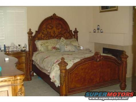 Bedroom scene with a large ornate wooden bed and matching dresser, window with blinds, and a fireplace