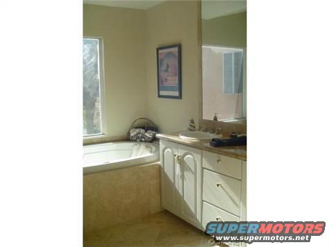 Bathroom with a bathtub, vanity, sink, and mirror. A framed picture hangs on the wall
