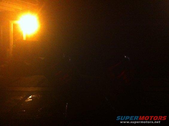 Dark scene with a car silhouette under a bright light, wet ground
