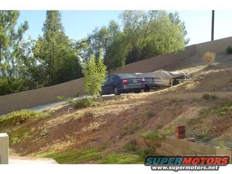 dark sedan parked next to a covered trailer on a sloped driveway