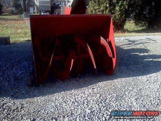 Red snow blower auger with visible blades, set on gravel