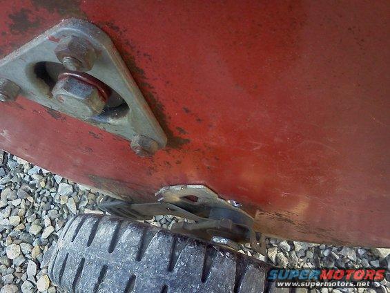 Red metal panel with a triangular bracket bolted on, a tire is visible below
