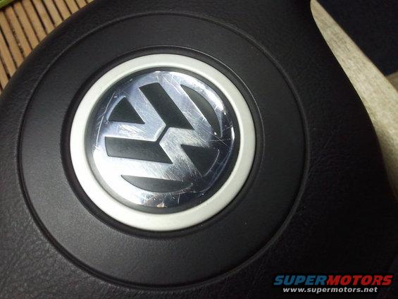 Close-up of a scratched Volkswagen logo on a black steering wheel