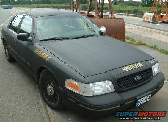 Black 2003 Ford Crown Victoria police car with gold "SHERIFF" text on the door and hood, parked on a road