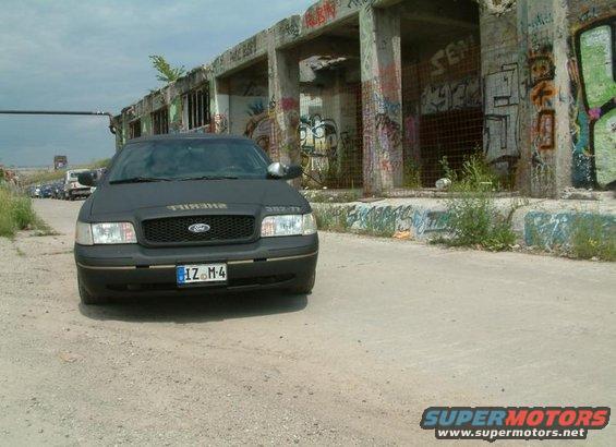 Front view of a black Ford Crown Victoria with 'SHERIFF' on the hood, parked in front of a graffiti-covered building
