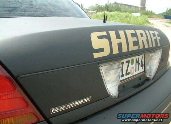 Dark colored Sheriff's vehicle rear, with gold 'SHERIFF' text and 'POLICE INTERCEPTOR' badge