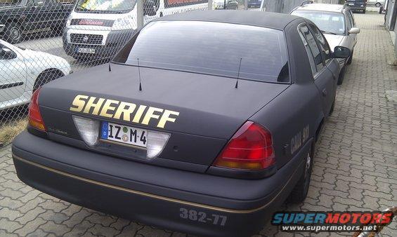 Black Ford Crown Victoria with 'SHERIFF' in gold on the trunk, parked next to other vehicles