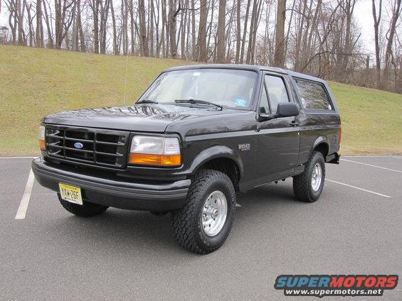 Black 1996 Ford Bronco parked on asphalt with trees and a grassy hill in the background