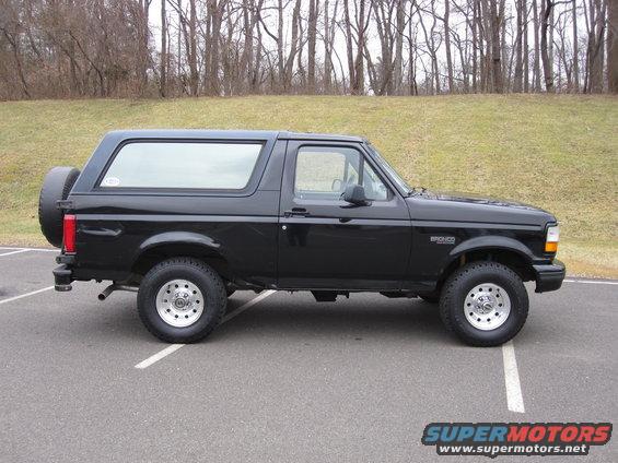 Black 1996 Ford Bronco SUV, side view, parked on asphalt with trees in background