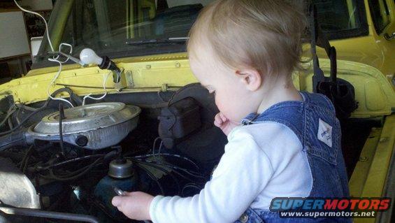 Yellow 1978 Ford Bronco engine bay with a toddler inspecting the motor