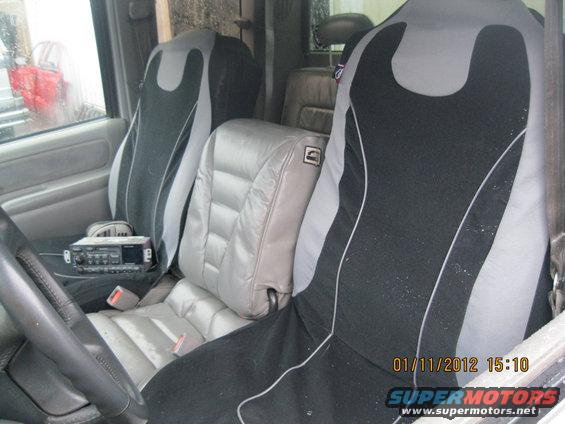Truck interior showing front seats with aftermarket covers, a center console with a radio, and a person visible through the driver's side window
