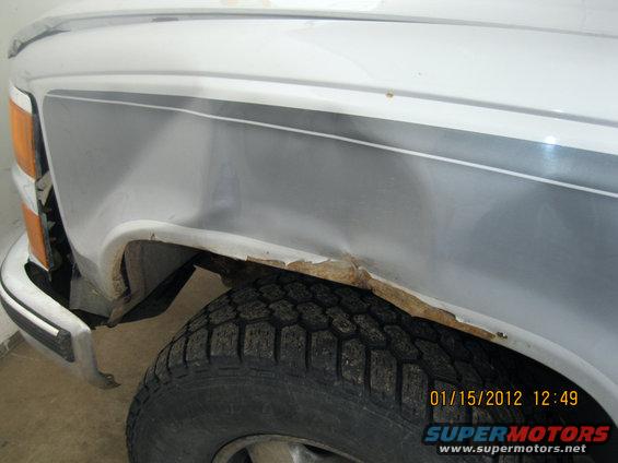 Close up of a white truck's front fender, showing rust around the wheel well and a two-tone stripe